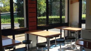 L’intérieur d’un restaurant, avec de nombreuses tables et des tabourets de bar, de grandes fenêtres et une vue sur l’extérieur.
