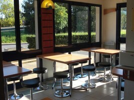 L’intérieur d’un restaurant, avec de nombreuses tables et des tabourets de bar, de grandes fenêtres et une vue sur l’extérieur.