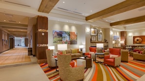 Een hotel lobby met een lange gang, een zithoek met fauteuils en banken, een open haard en kunst aan de muren.