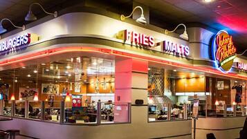 A restaurant with a curved counter, illuminated signs for 'FRIES MALTS' and 'Johnny Rockets', and a view into the kitchen area.