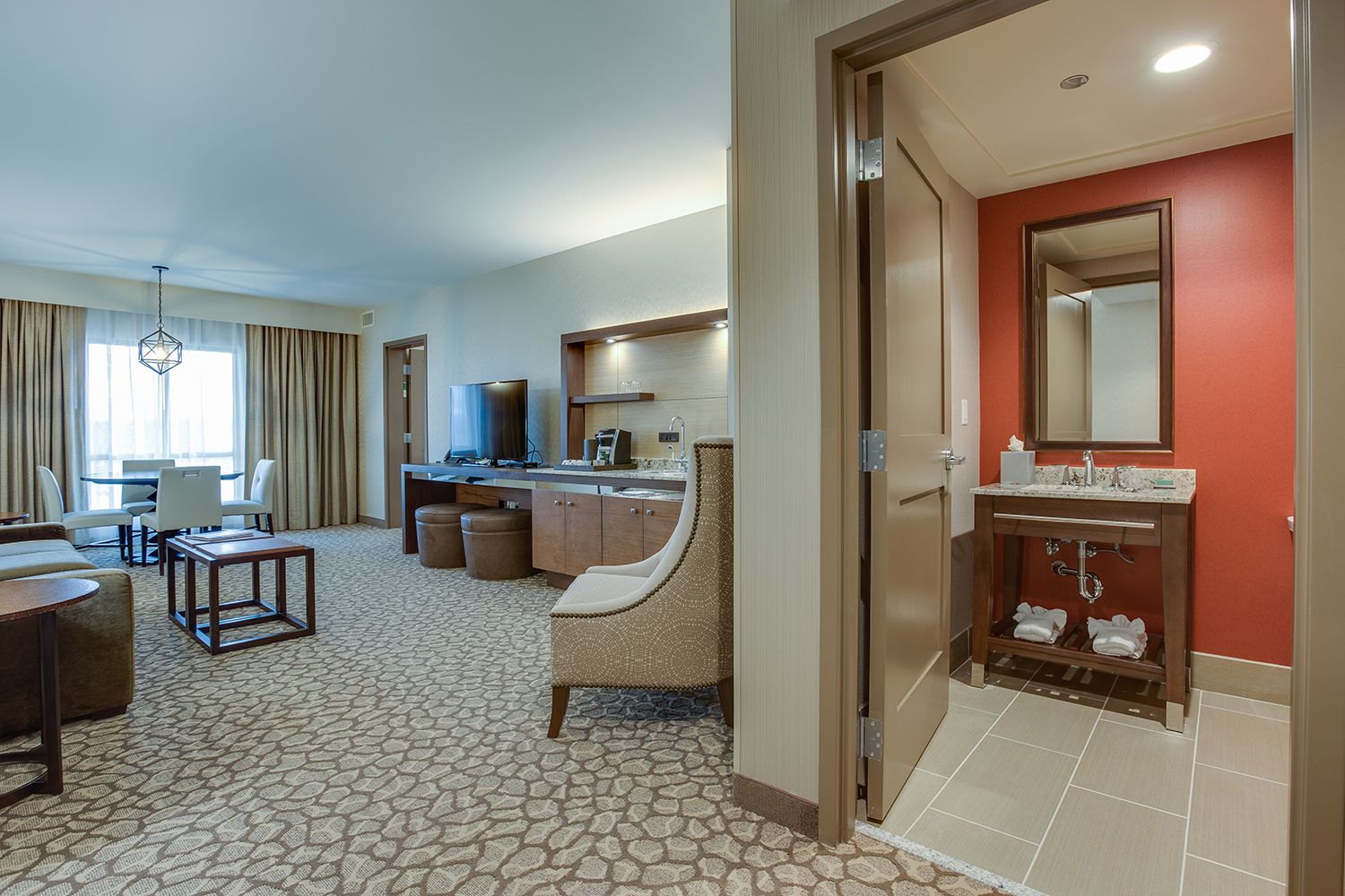 Une chambre d’hôtel comprenant un coin repas, une kitchenette, une salle de bain avec un miroir et un porte-serviettes, ainsi qu’une moquette à motifs.