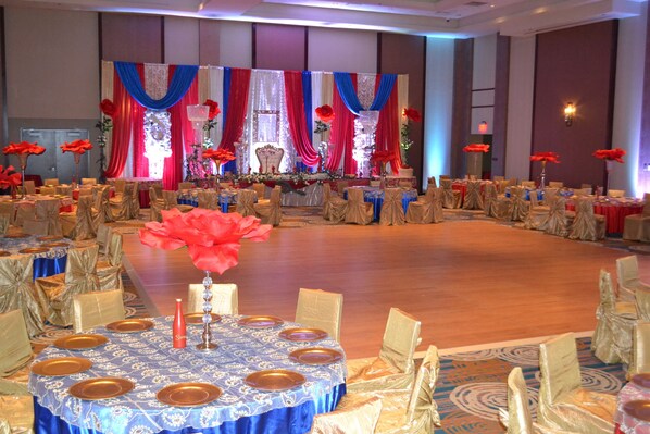 Une salle de banquet avec des tables rondes recouvertes de nappes bleues, des chaises dorées et des fleurs rouges.