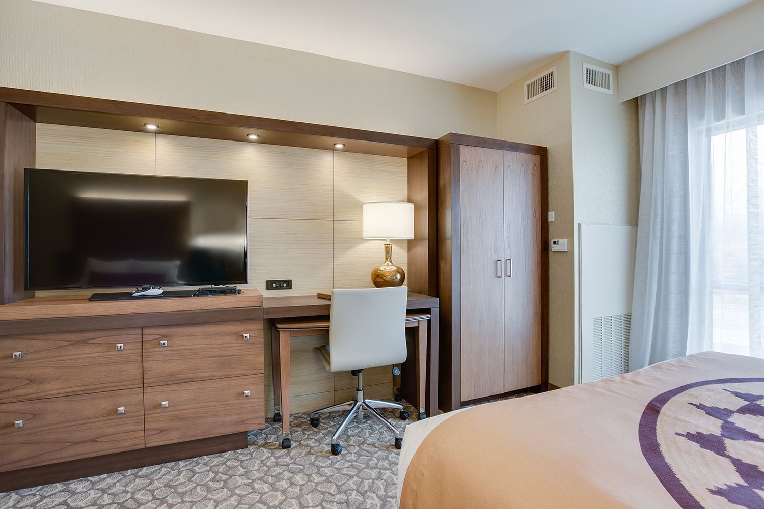 Una habitación de hotel con cama, escritorio con silla, televisión, armario y lámpara.