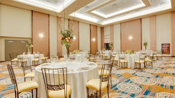 Een feestzaal met ronde tafels gedekt voor een diner, met witte tafelkleden en gouden stoelen.