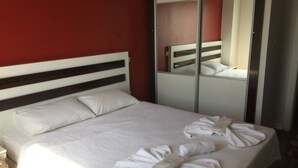 A neatly made bed with white linens and towels, a wooden headboard, and a mirror on the wall. - Tuyap Apartments (Istanbul)