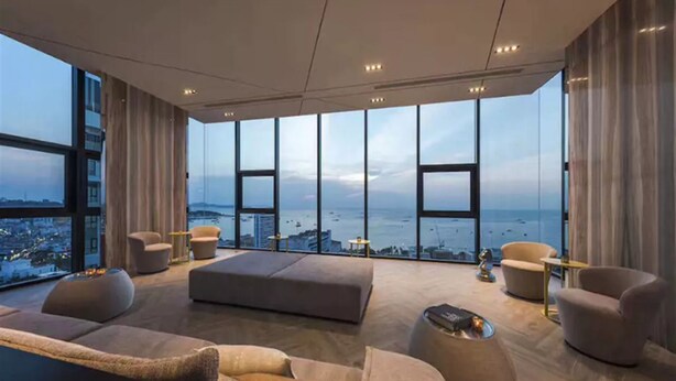 A spacious living room with a large window overlooking a cityscape and the sea. There are multiple seating areas, including sofas and armchairs. - The base pattaya condo (Pattaya)