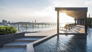 A rooftop pool area with a view of the city skyline, a covered seating area, and steps leading down to the water. - The base pattaya condo (Pattaya)