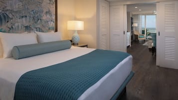 Habitación de hotel con una cama grande, una mesita de noche con lámpara, un cuadro en la pared y vistas al balcón a través de la puerta.