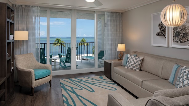 Ein geräumiges Wohnzimmer mit Balkon, Deckenventilator und großem Fenster mit Blick auf den Ozean.