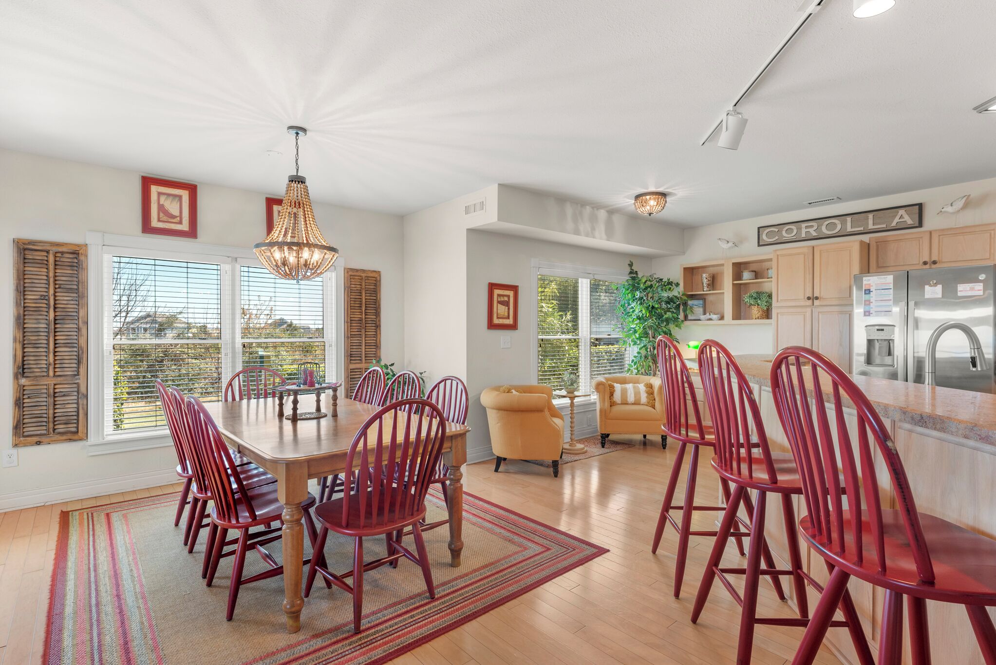 A spacious dining area with a wooden table and red chairs, a kitchen with wooden cabinets, and a large window with blinds.