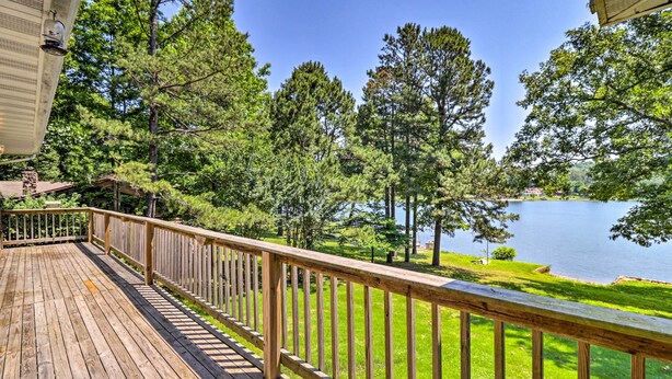 Una terraza de madera con barandilla que da a un lago y árboles.