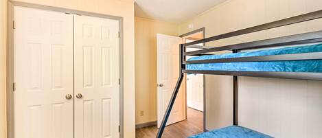 Une pièce avec un lit superposé, une porte blanche et un couloir menant à une autre pièce.