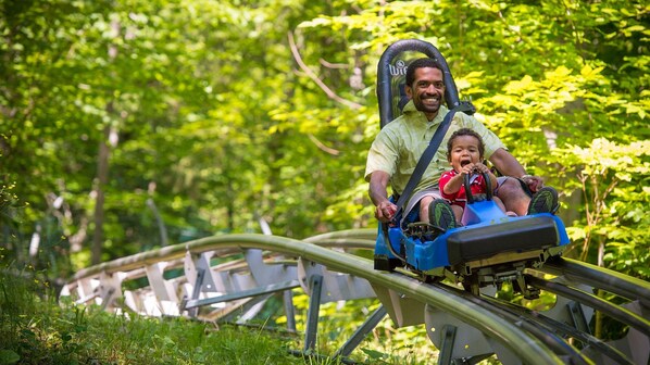A man and a child on a small blue vehicle on a curved track surrounded by greenery.