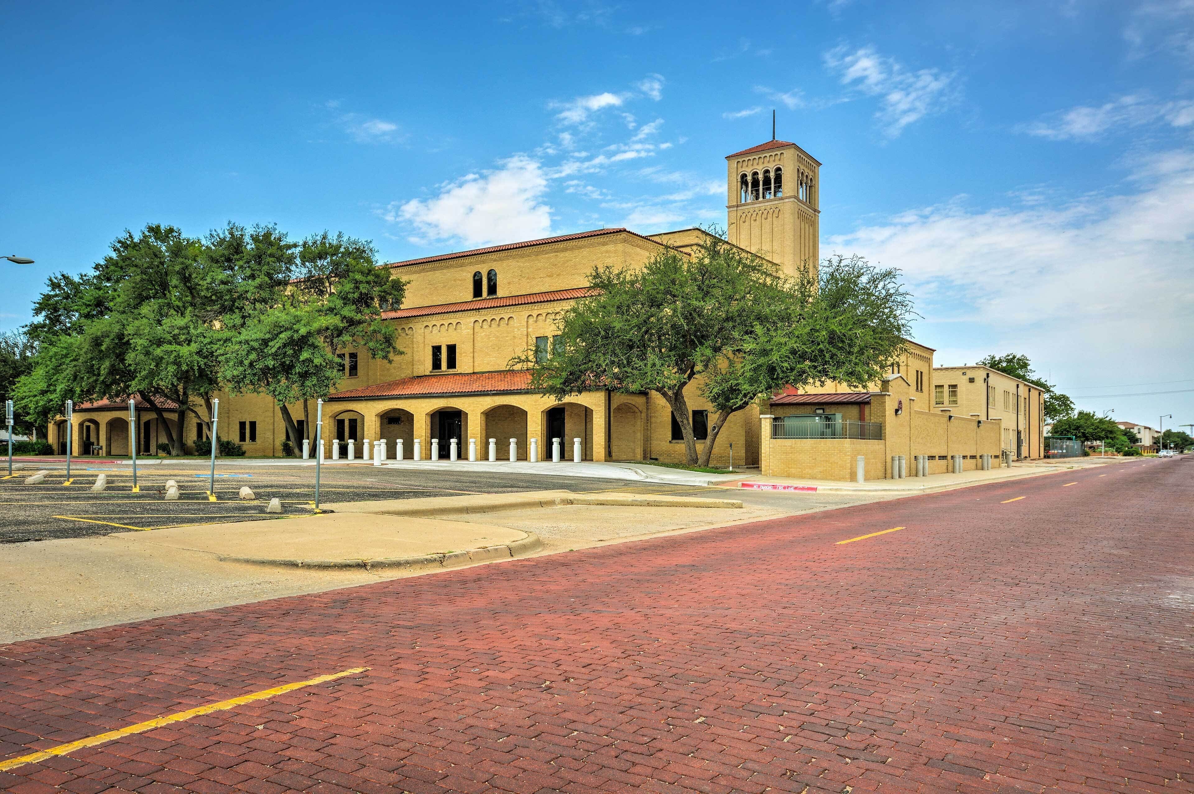 A historic building with a prominent tower, arched windows, and a paved street in front.