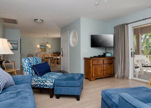 Una sala de estar con un sofá, un reposapiés y un televisor sobre un mueble de madera.