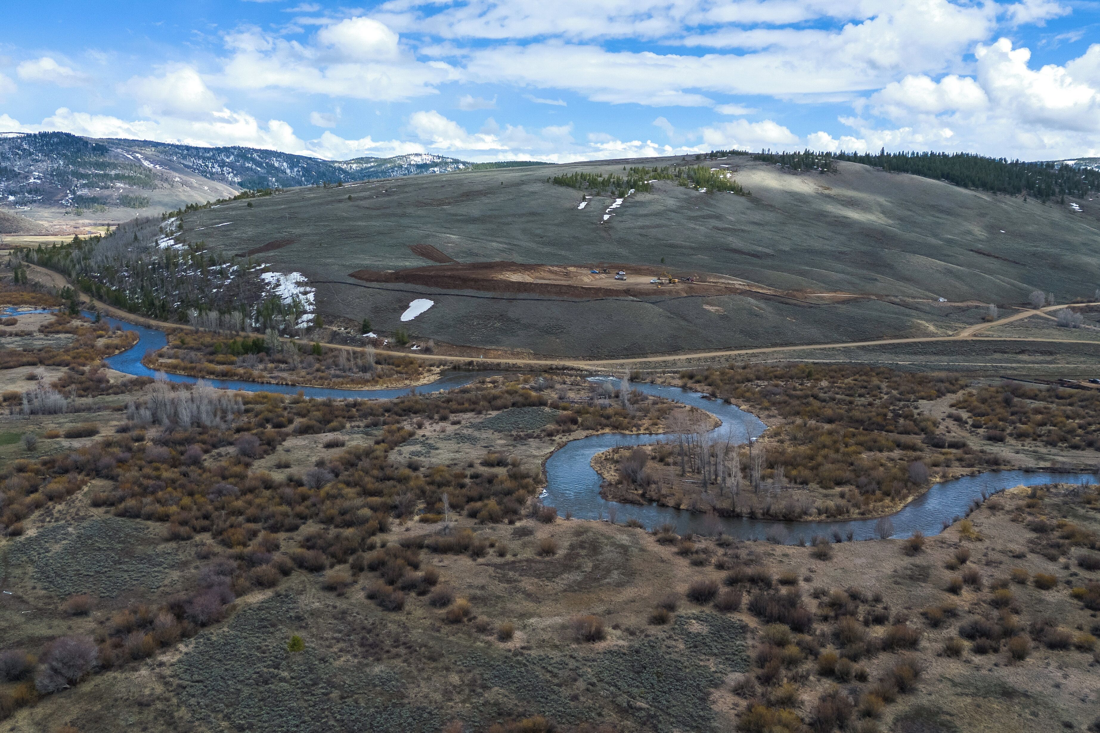 Un vaste paysage caractérisé par une rivière sinueuse, un chemin de terre et un terrain vallonné à la végétation clairsemée.