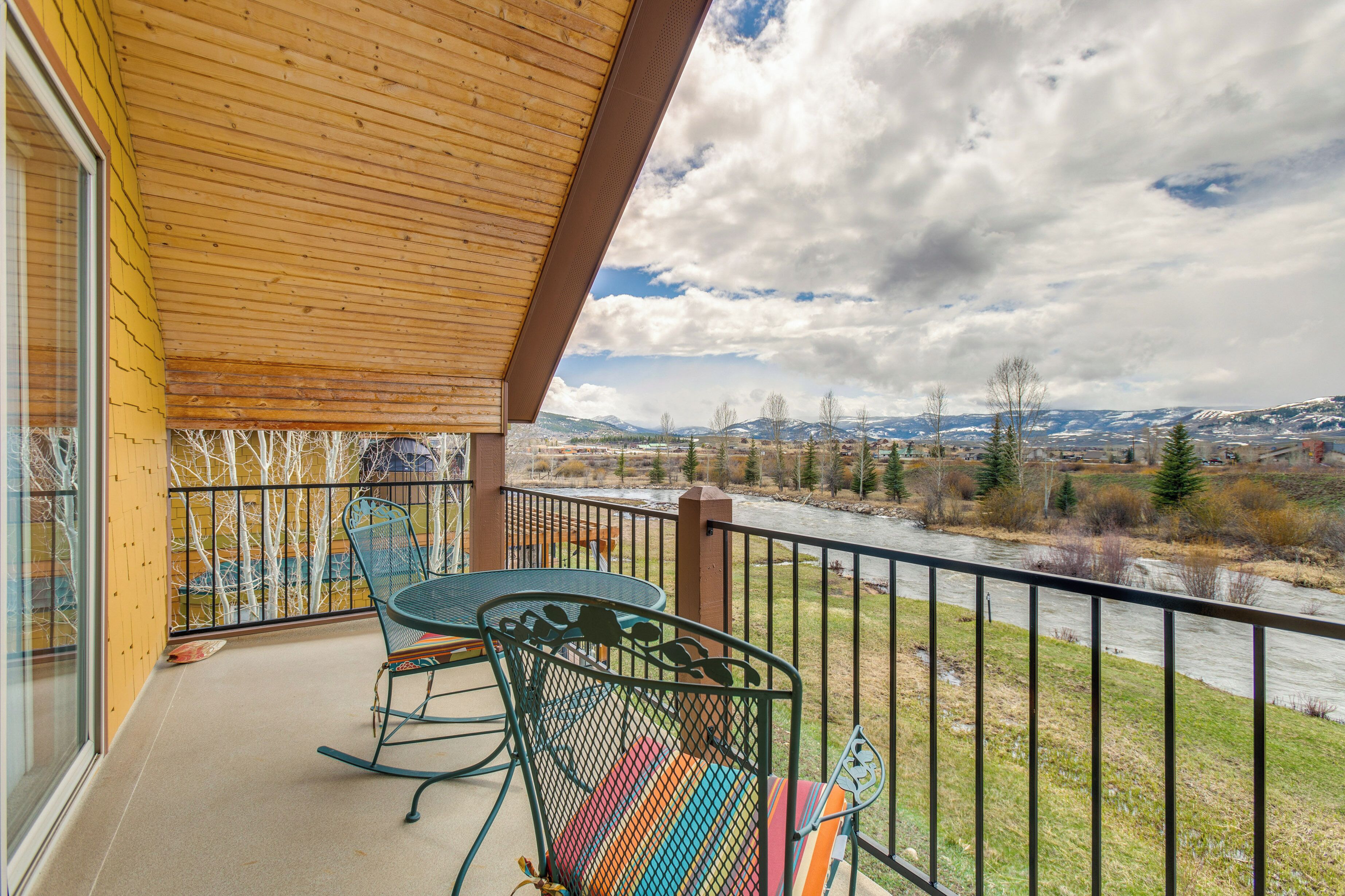 A balcony with a view of a river and mountains, equipped with metal chairs and a table.