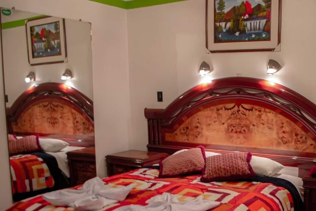 Une chambre dotée d’un grand lit, d’une tête de lit en bois, d’une table de chevet, d’un miroir et de deux lampes fixées au mur.