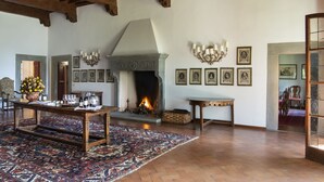 Ein geräumiges Zimmer mit Kamin, Holzbalken, einem Esstisch mit Weingläsern und gerahmten Bildern an der Wand.