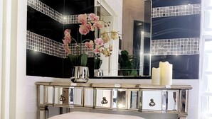 A vanity with a mirror, a vase with flowers, and a bench.