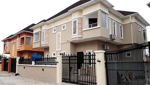 A two-story house with a gated entrance, a satellite dish, and a visible air conditioning unit.