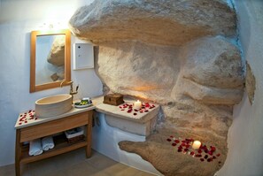 Une salle de bain avec un mur en pierre, un meuble-lavabo en bois, un miroir et une bougie allumée.