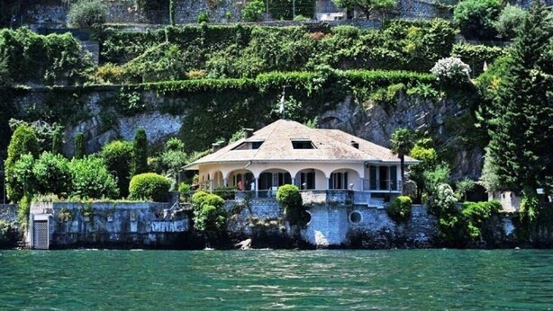 A coastal villa with a tiled roof, surrounded by lush greenery and a stone wall.