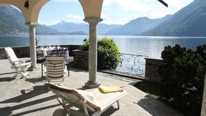 A terrace with lounge chairs, a table set for dining, and a view of a lake with mountains in the background.