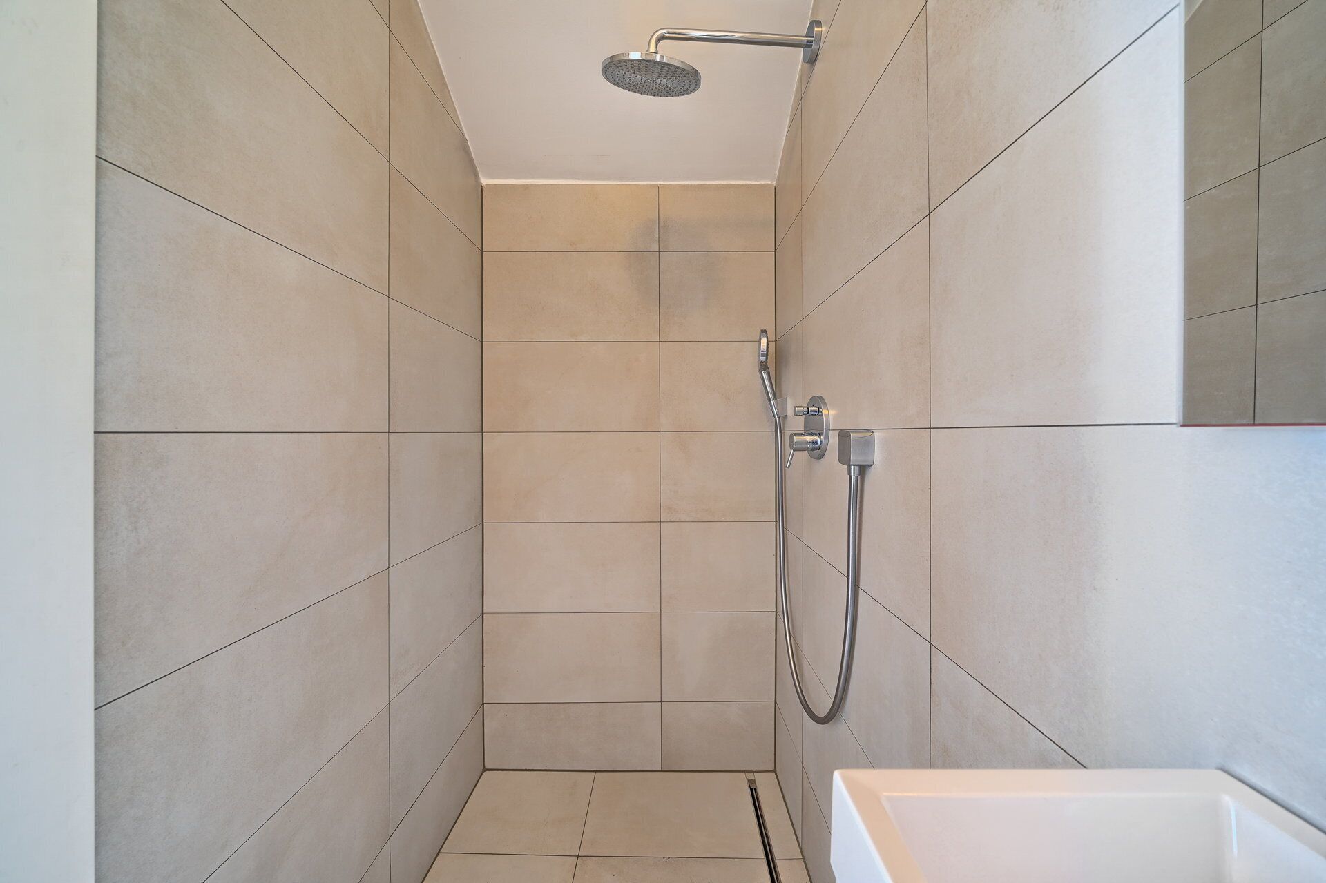 A small, tiled shower room with a handheld showerhead and a wall-mounted faucet.