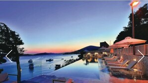 An infinity pool with lounge chairs and umbrellas, overlooking a calm body of water with boats. - Beachfront Villa Deep Blue with Pool I (Trogir)