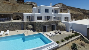 A white villa with a swimming pool, stone walls, and a hillside view. - Villa DeLucien (Mykonos)