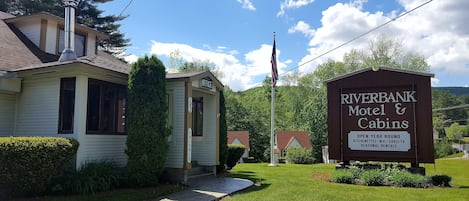 A Riverbank Motel & Cabins with a sign indicating open year-round, seasonal rentals, and amenities like kitchenettes, WiFi, and cable TV.