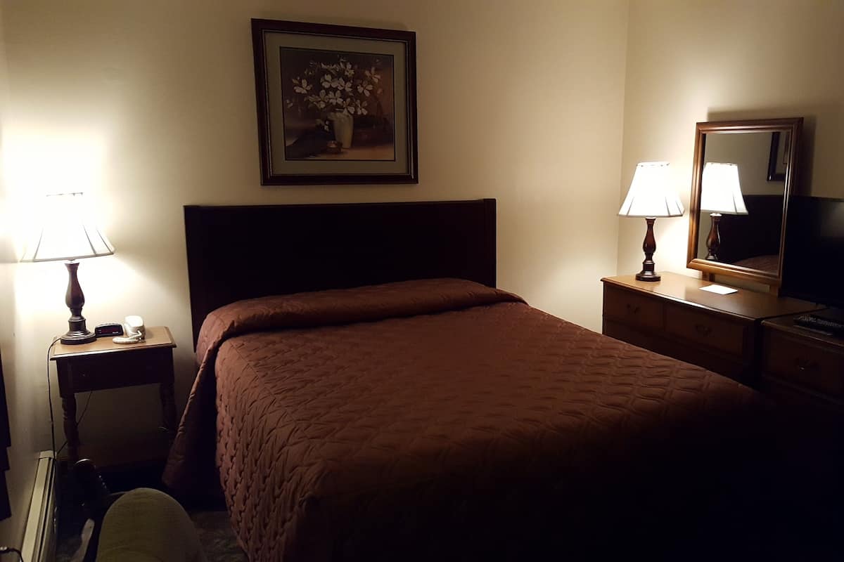 Ein Hotelzimmer mit einem großen Bett, einem Nachttisch mit Lampe, einem Schminktisch mit Spiegel und einem Fernseher.