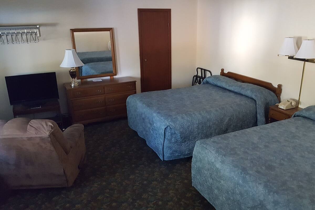 Ein Hotelzimmer mit zwei Betten, einem Schminktisch, einem Fernseher, einem Spiegel und einer Lampe.