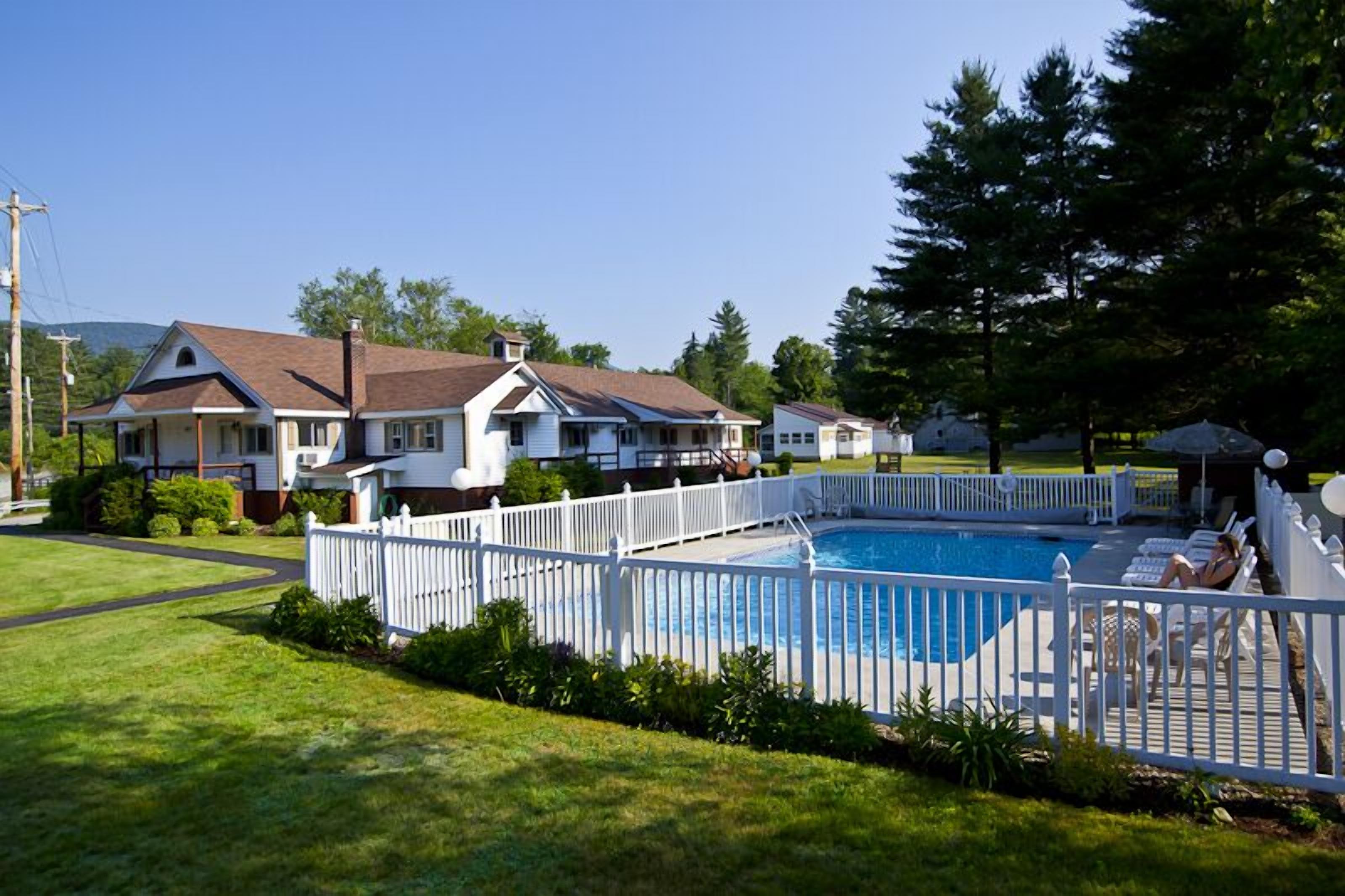 A residential area with a swimming pool surrounded by a white fence, houses in the background, and a clear sky.