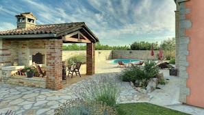 A stone patio with a pool, outdoor seating, and a garden area.