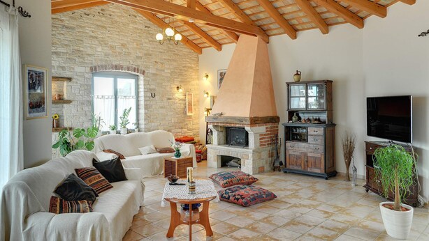 A cozy living room with a stone wall, wooden beams, a fireplace, and a television.