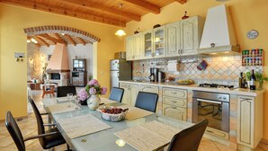 A spacious kitchen with wooden beams, a dining area with a glass table, and a tiled backsplash.