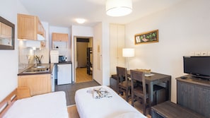 Hotellihuone, jossa on kaksi sänkyä, pieni keittiö, ruokailutila ja televisio.