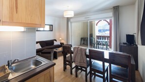 A compact kitchen with a sink and wooden cabinets, a sofa with a lamp, and a dining area with chairs and a table. - Les Jardins de Balnea Loudenvielle 4PD10 (Loudenvielle)