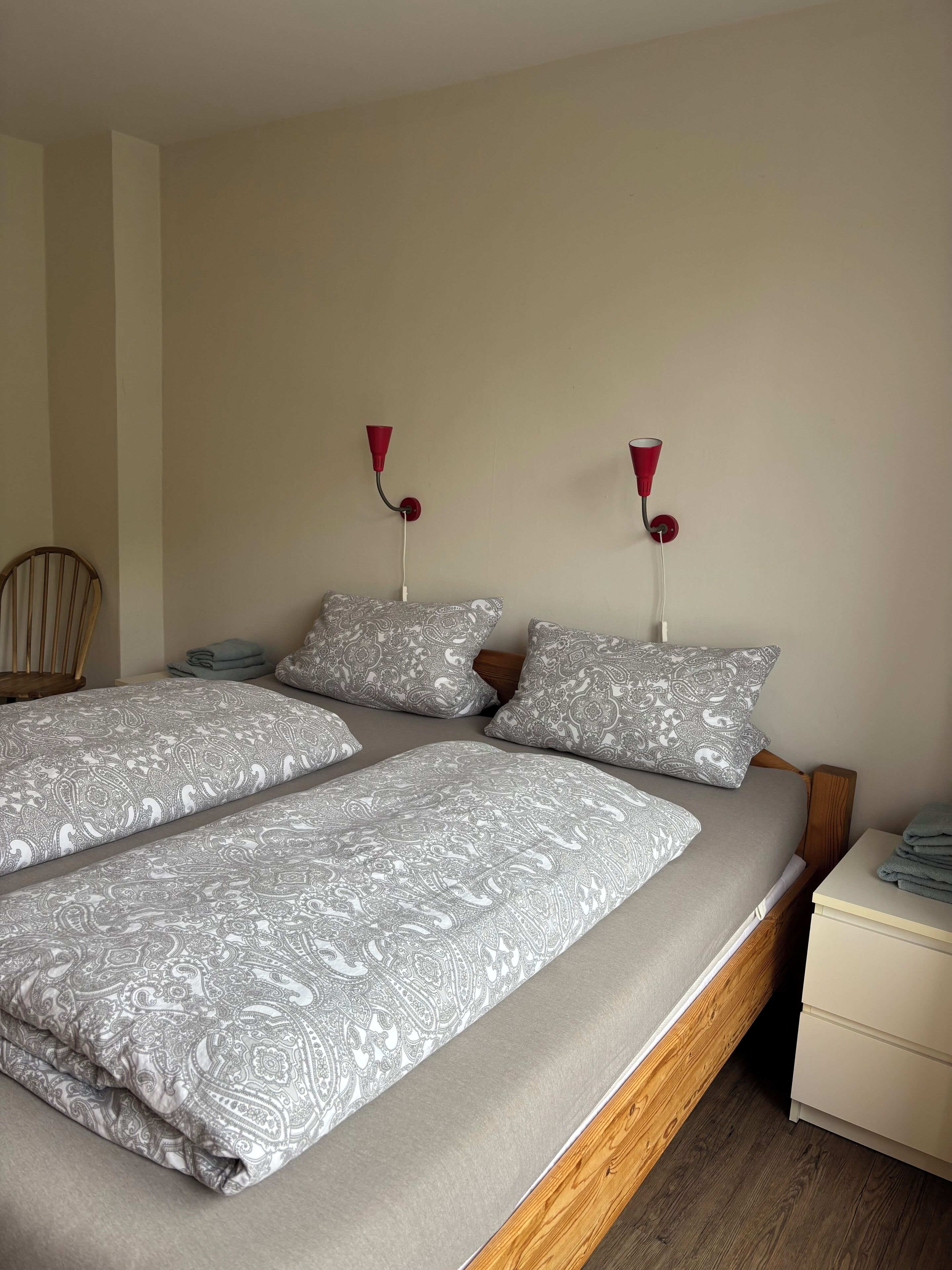 A double bed with patterned bedding, two bedside tables, a chair, and wall-mounted lamps.