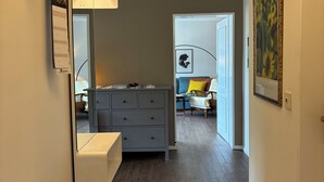 A hallway with a wooden floor, a grey dresser, a white wall-mounted shelf, and a framed picture.