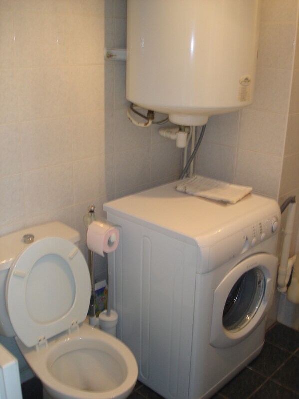 A compact bathroom with a toilet, washing machine, and a sink.