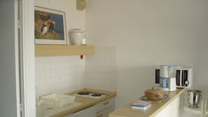Eine kleine Küche mit Spüle, Herd und Mikrowelle. Oberhalb des Herdes befindet sich ein Regal mit ein paar Gegenständen.