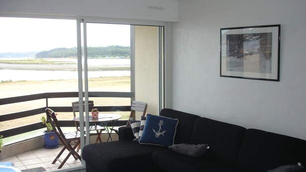 Ein Balkon mit Blick auf Strand und Meer, ein schwarzes Sofa, ein kleiner Tisch und ein Sessel.
