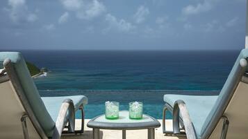 A balcony with two lounge chairs and a small table with two glasses of water.