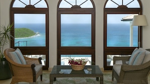 Habitación con vistas al océano, que incluye un ventilador de techo, muebles de mimbre y una mesa con una cesta y flores.