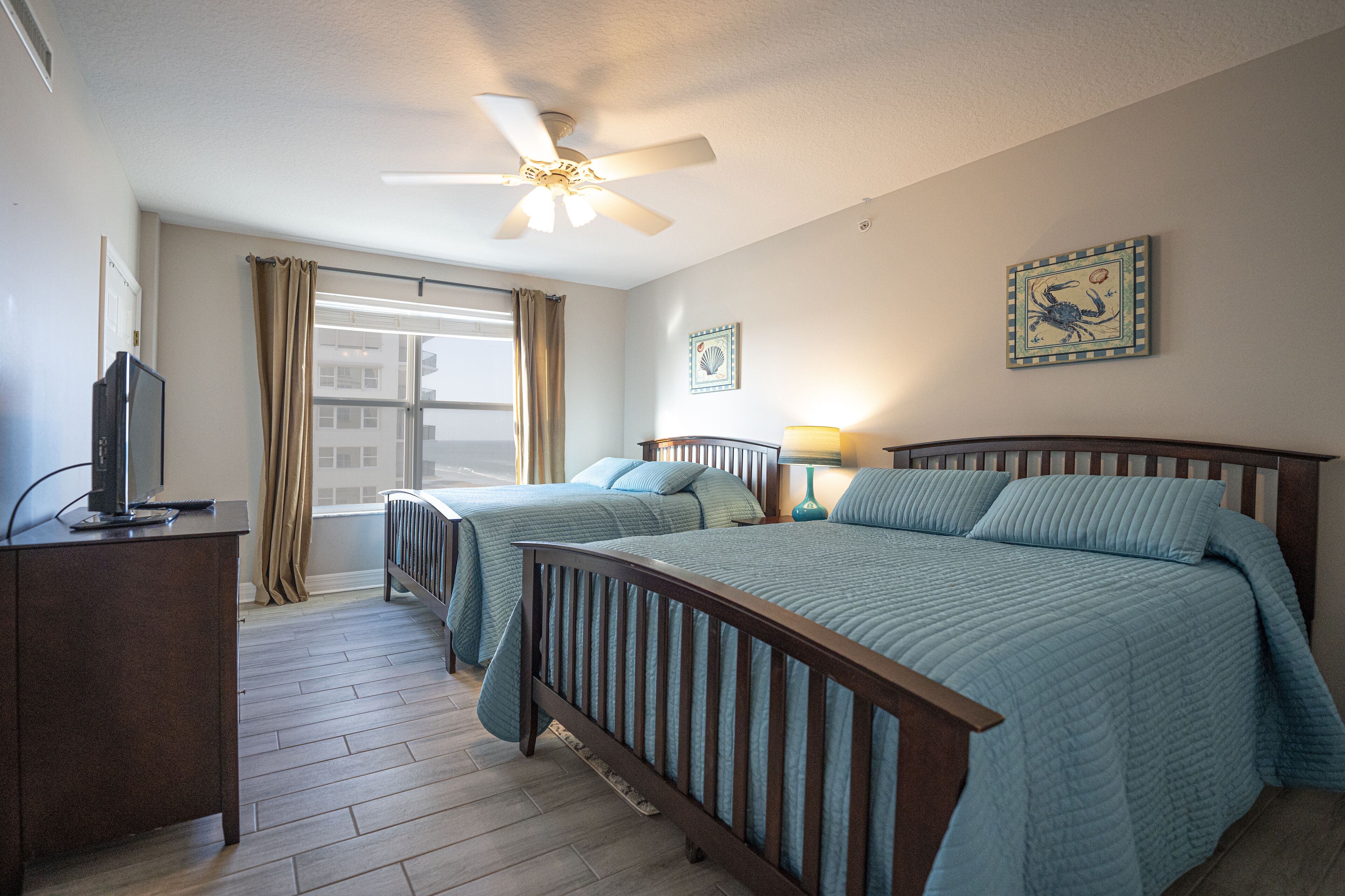 A hotel room with two beds, a ceiling fan, a TV, and a window with curtains.