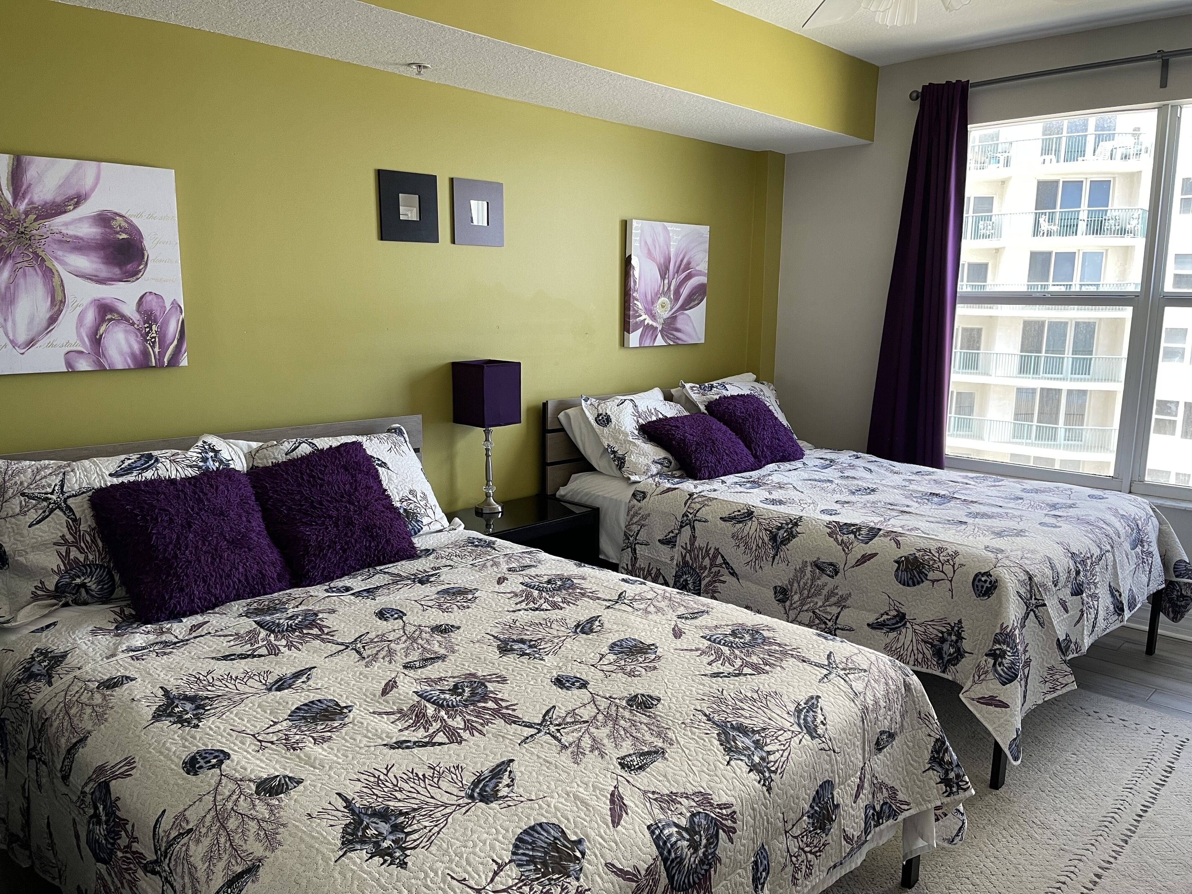 Een hotelkamer met twee bedden, bloemenbeddengoed, een nachtkastje met een lamp en kunstwerken aan de muur.