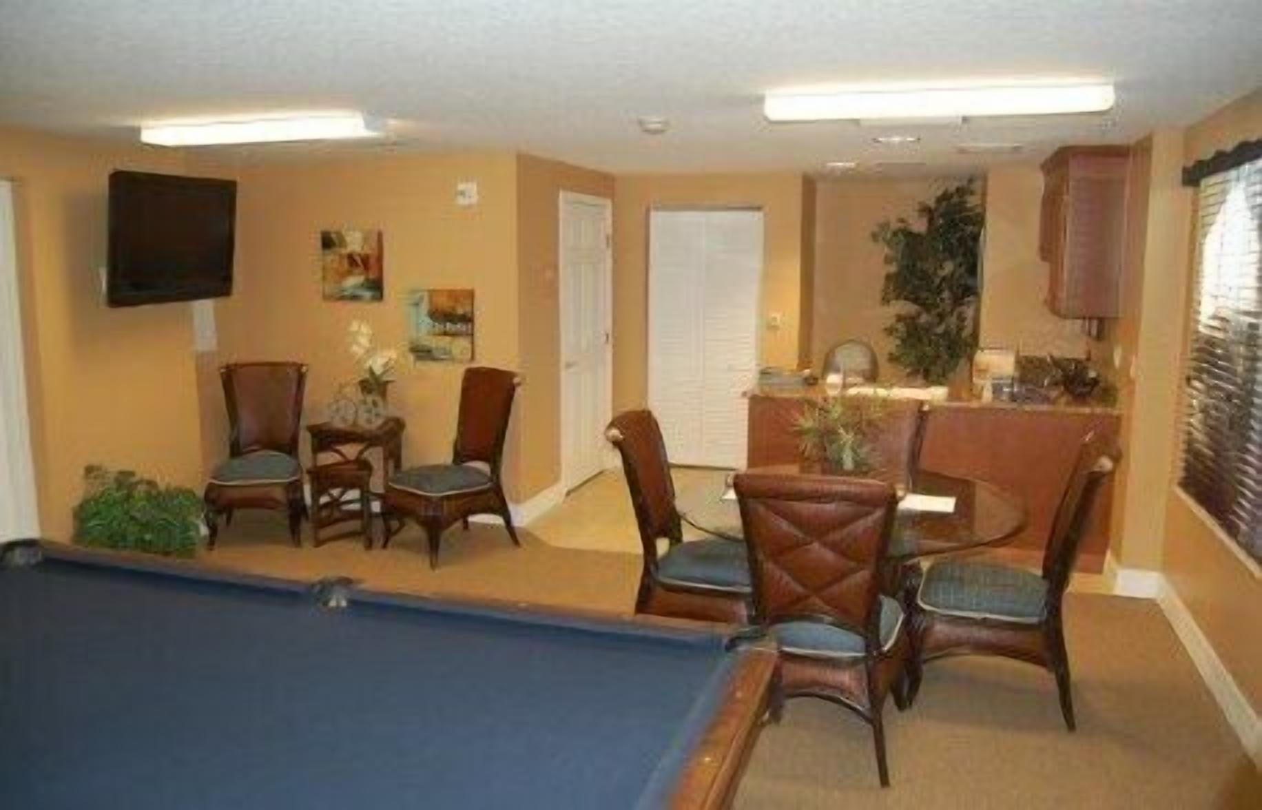 A room with a pool table, dining area with chairs, a television mounted on the wall, and a door leading to another room.